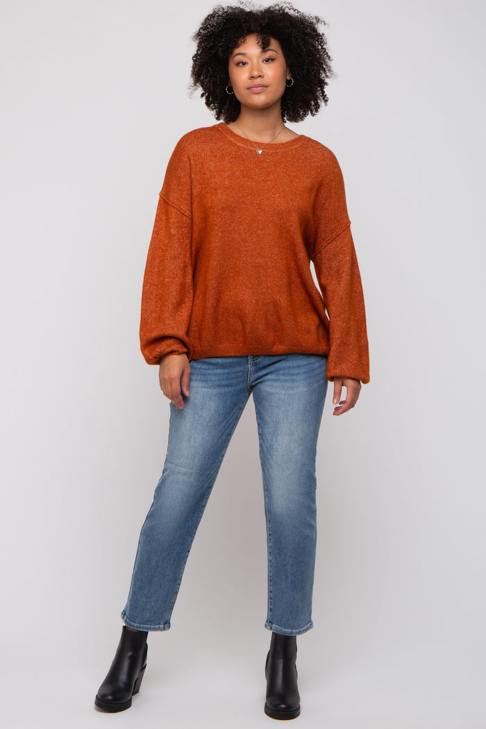 woman wearing an oversized burnt orange sweater with balloon sleeves and paired with light wash straight leg jeans and black ankle boots