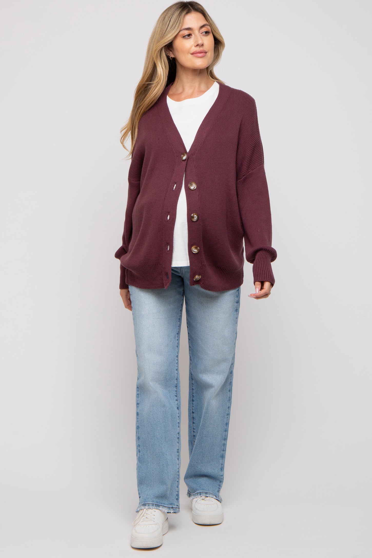 woman wearing a burgundy maternity cardigan over a white top and light blue jeans, showing her baby bump