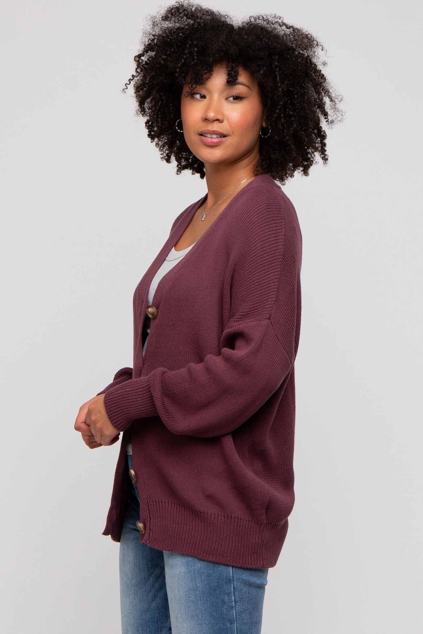 woman wearing a burgundy cardigan with a loose fit and button detail, styled with a gray top and blue jeans