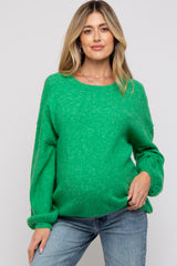 woman wearing a green oversized maternity sweater and showing her baby bump