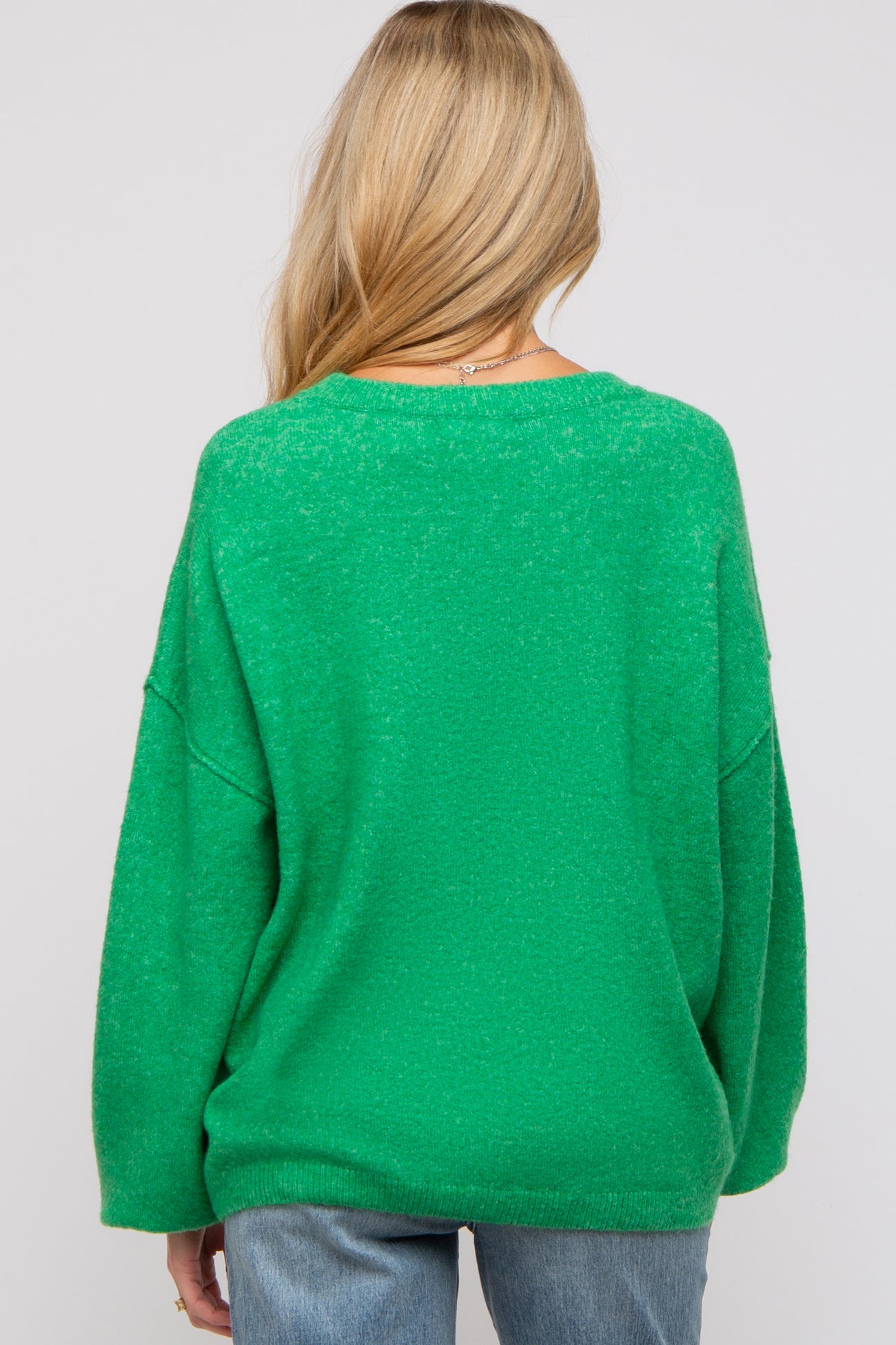 woman wearing a green oversized maternity sweater with a relaxed fit and slouchy sleeves