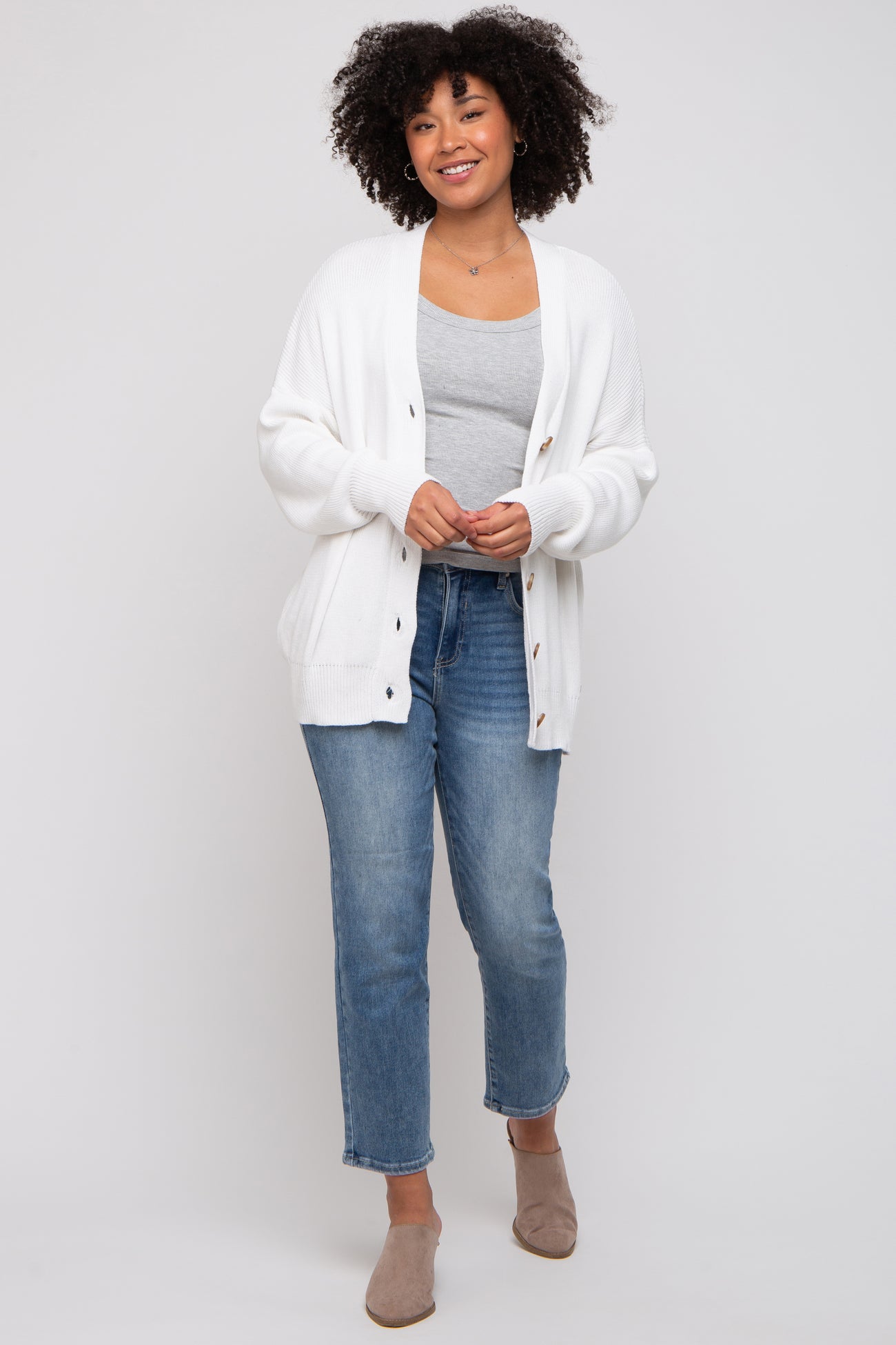woman wearing a white knit cardigan over a gray tank top, paired with light blue jeans and beige slip-on shoes