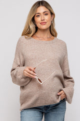 woman wearing a beige maternity sweater with long sleeves and holding sunglasses
