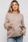woman wearing a beige maternity sweater with long sleeves and holding sunglasses