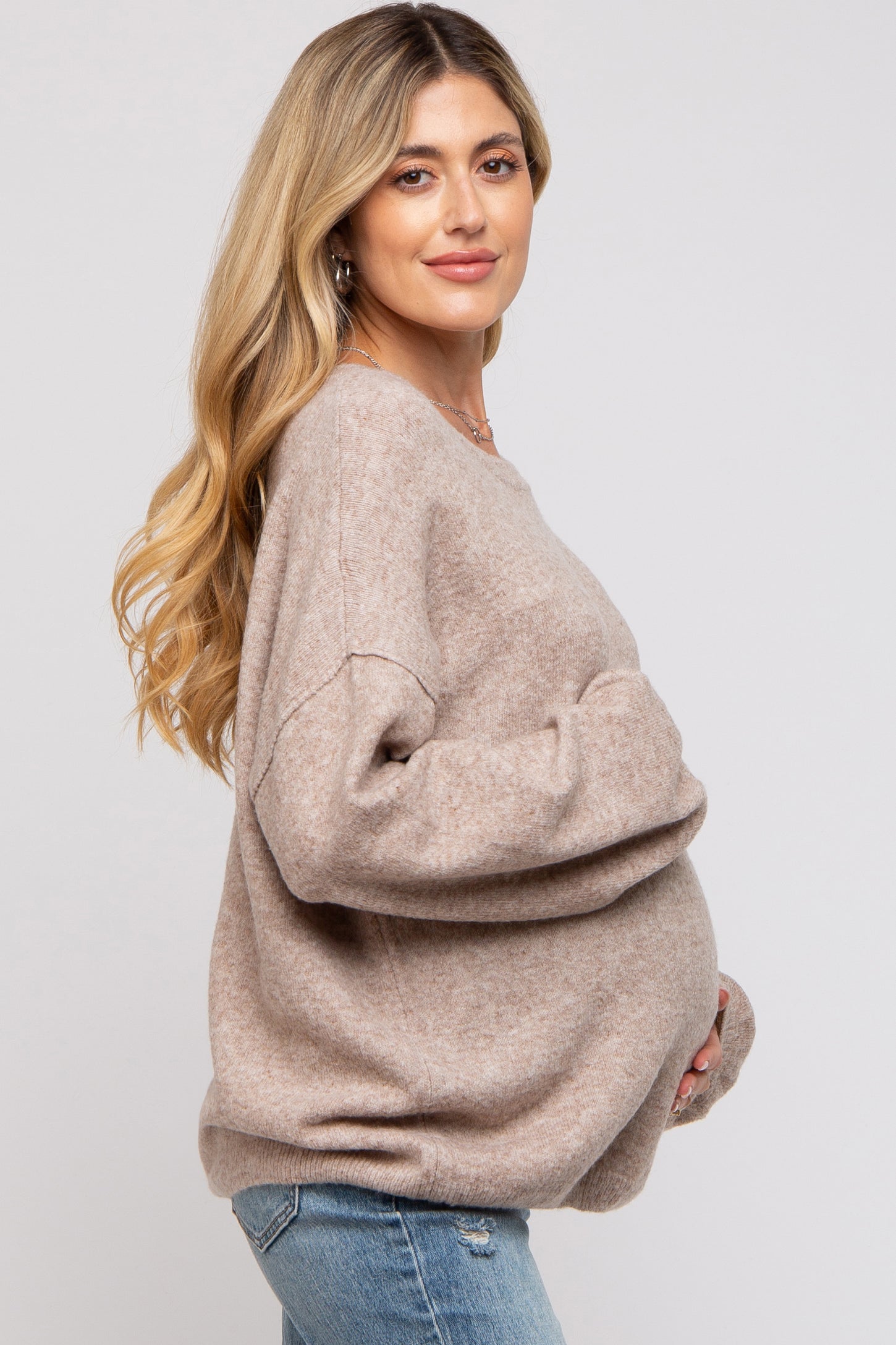 woman wearing a taupe oversized maternity sweater and holding her baby bump