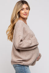 woman wearing a taupe oversized maternity sweater and holding her baby bump