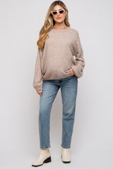 woman wearing a soft beige oversized maternity sweater and light blue jeans, holding her baby bump