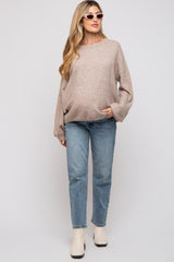 woman wearing a beige oversized maternity sweater and blue jeans, with a visible baby bump and sunglasses