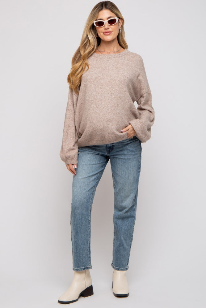 woman wearing a soft beige oversized maternity sweater and light blue jeans, holding her baby bump