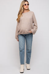 woman wearing a beige oversized maternity sweater and blue jeans, with a visible baby bump and sunglasses