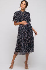 woman wearing a navy floral printed maternity dress with short sleeves and pleated skirt, holding her baby bump