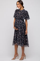 woman wearing a black floral knee-length maternity dress with flutter sleeves and holding her baby bump
