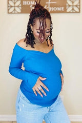 woman wearing a bright blue off-shoulder maternity top and holding her baby bump with a smile