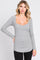 woman wearing a light grey ribbed long sleeve top with a scoop neckline and curved hem, posing confidently