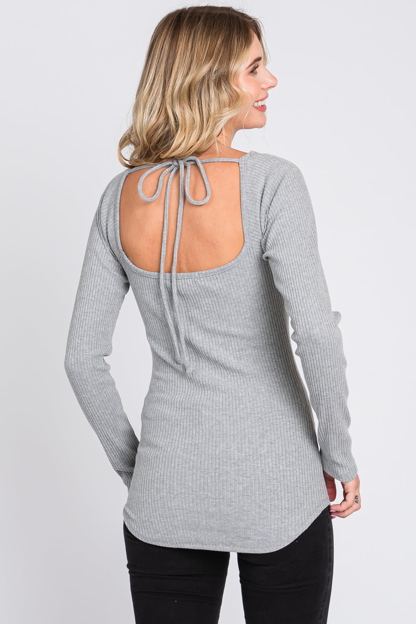 woman wearing a light gray ribbed long sleeve top with a tie-back detail and a curved hemline