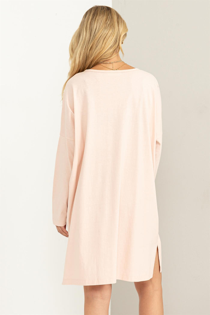 woman wearing a light pink oversized sweater dress with side slits and long sleeves, viewed from the back