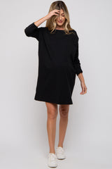 woman wearing a black maternity dress with three-quarter sleeves and a relaxed fit, holding her hand to her forehead