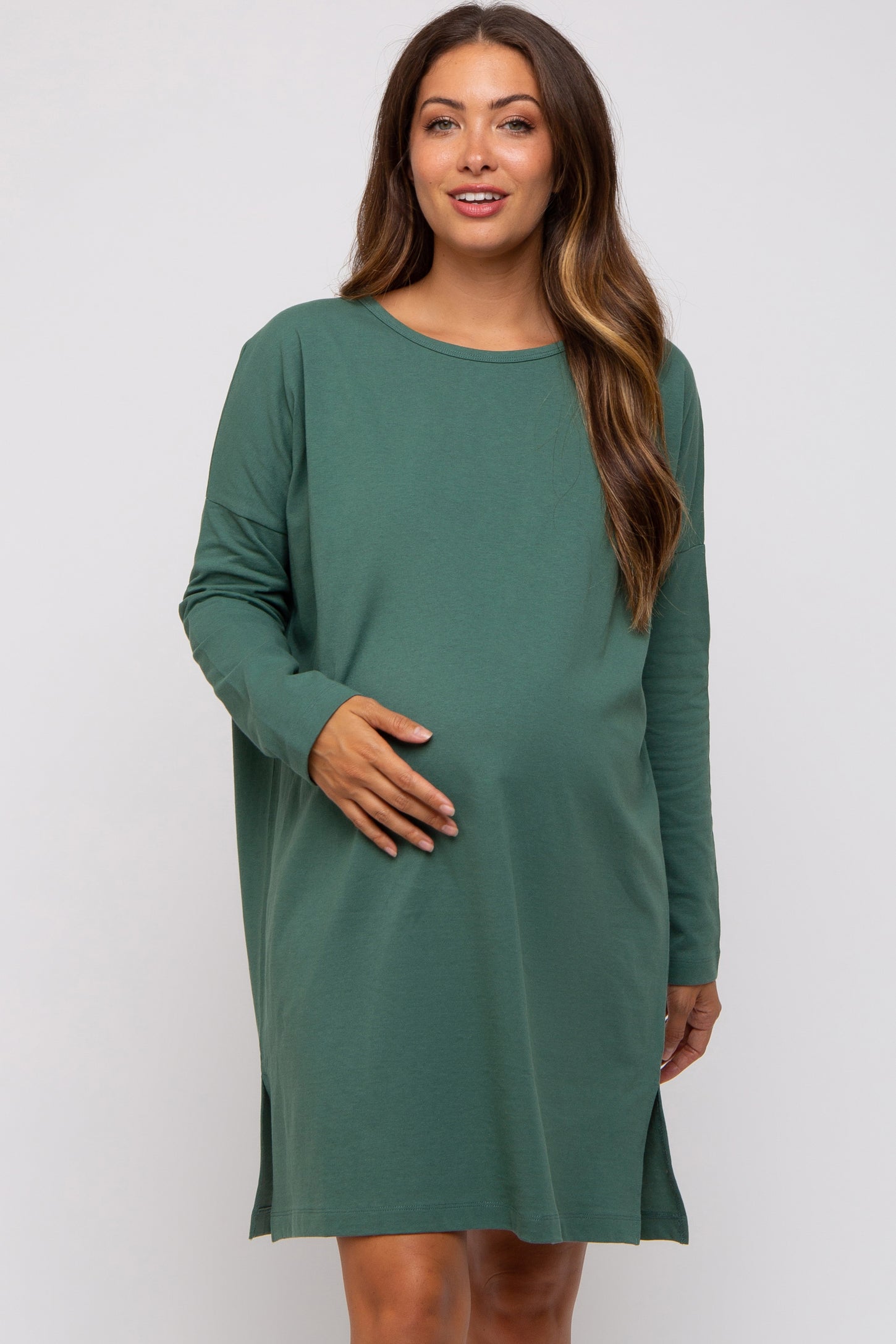 woman wearing a green long sleeve maternity dress and gently holding her baby bump