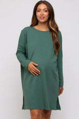 woman wearing a green long sleeve maternity dress and gently holding her baby bump