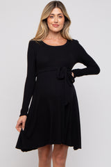woman wearing a black long sleeve maternity dress with a tie waist and flared skirt, showing her baby bump