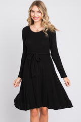 woman wearing a black long sleeve ribbed dress with a tie waist detail and a flared skirt