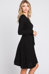 woman wearing a black long sleeve wrap dress with a tie waist detail and a flared skirt