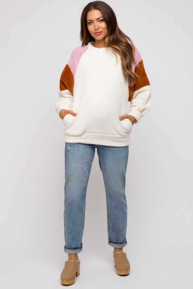 woman wearing a cream oversized maternity sweatshirt with color-blocked sleeves and denim jeans, hands in pockets