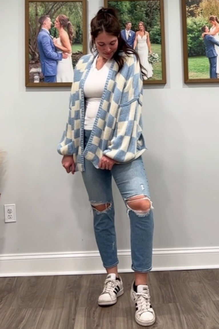 woman wearing a light blue and white checkered cardigan over a white top and distressed jeans with sneakers
