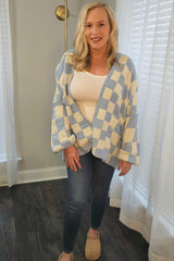 woman wearing a blue and cream checkered oversized cardigan with a white tank top and jeans, standing indoors