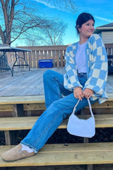 woman wearing a blue and white patterned cardigan, white t-shirt, and high-waisted jeans, sitting on wooden steps