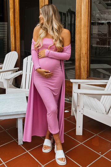 woman wearing a pink ribbed off-shoulder maternity dress with a long duster, holding her baby bump