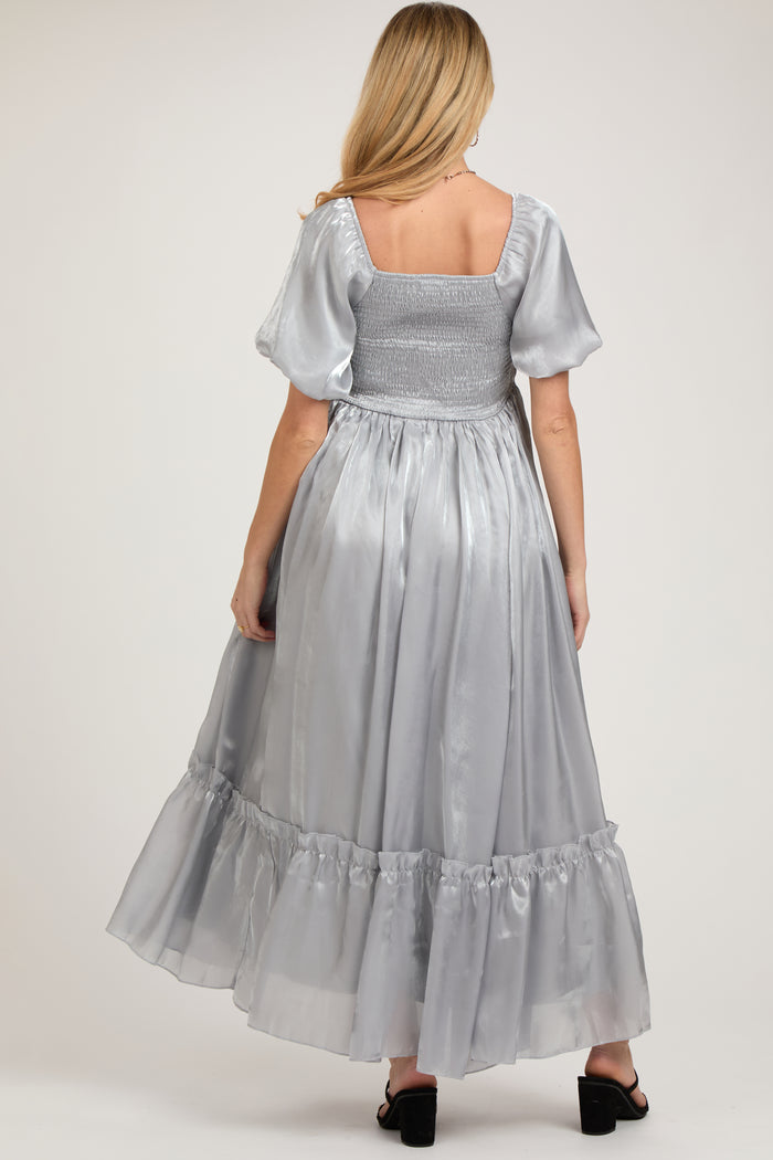 woman wearing a silver maternity maxi dress with puff sleeves and a smocked bodice, showcasing her baby bump from the back