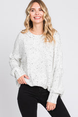 woman wearing a white speckled oversized sweater and black skinny jeans, smiling against a plain background