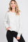 woman wearing a white speckled oversized sweater and black skinny jeans, smiling against a plain background