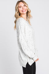 woman wearing a light gray speckled oversized sweater with a side slit, smiling and facing to the side