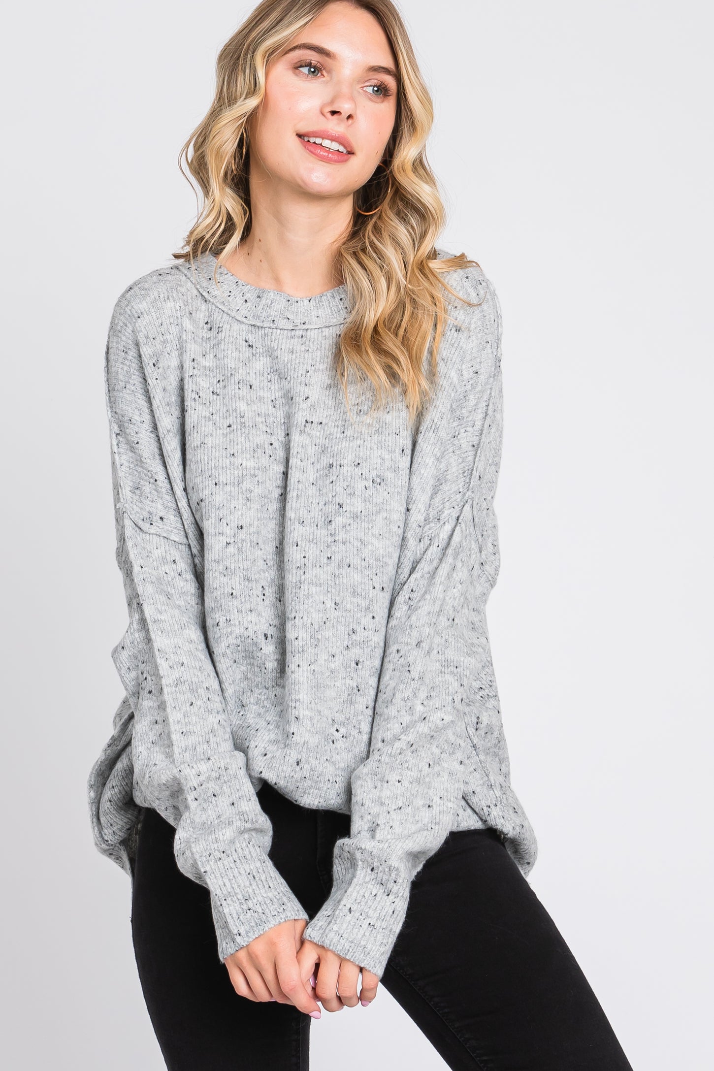 woman wearing a light gray oversized knitted sweater with a relaxed fit and speckled detailing, paired with black jeans