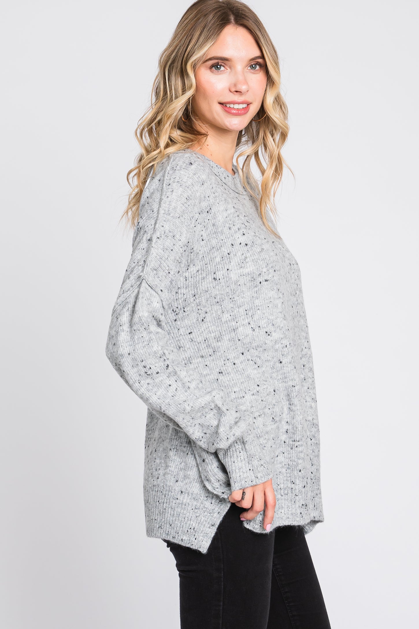 woman wearing a gray oversized sweater with a textured finish and side slits, styled with black skinny jeans