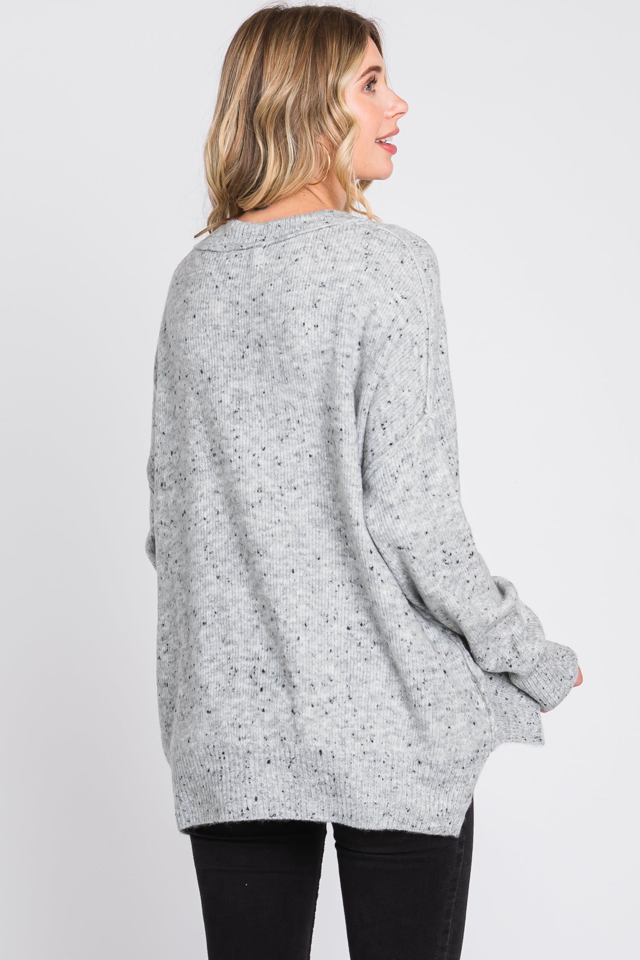 woman wearing a light gray oversized sweater with a speckled texture, view from the back