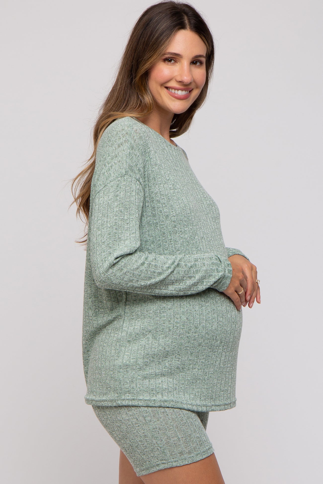 woman wearing a light green maternity knit top and shorts, showing her baby bump