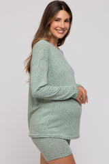 woman wearing a light green maternity knit top and shorts, showing her baby bump