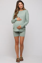 woman wearing a light green maternity short set with a textured design, gently cradling her baby bump