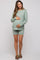 woman wearing a light green maternity short set with a textured design, gently cradling her baby bump