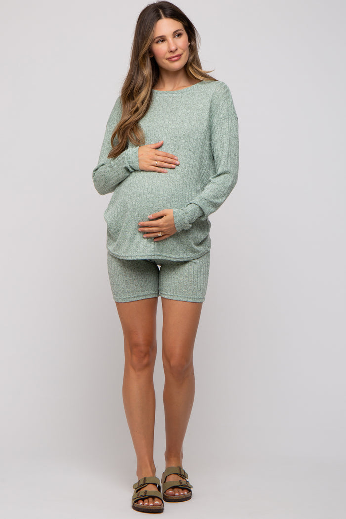 woman wearing a light green maternity short set with a textured design, gently cradling her baby bump