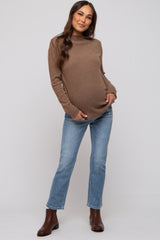 woman wearing a brown maternity sweater and blue jeans, showing her baby bump, standing in a casual pose