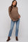woman wearing a brown maternity sweater and blue jeans, showing her baby bump, standing in a casual pose