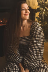 woman wearing a black and white checkered puff sleeve dress, sitting in front of a decorated Christmas tree