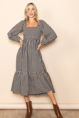 woman wearing a black and white checkered long sleeve midi dress with puff sleeves and a tiered skirt, posing confidently
