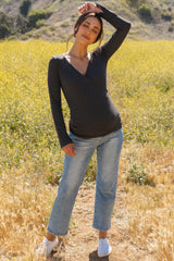 woman wearing a dark gray long sleeve maternity top with a crossover design and light blue jeans, standing in a field