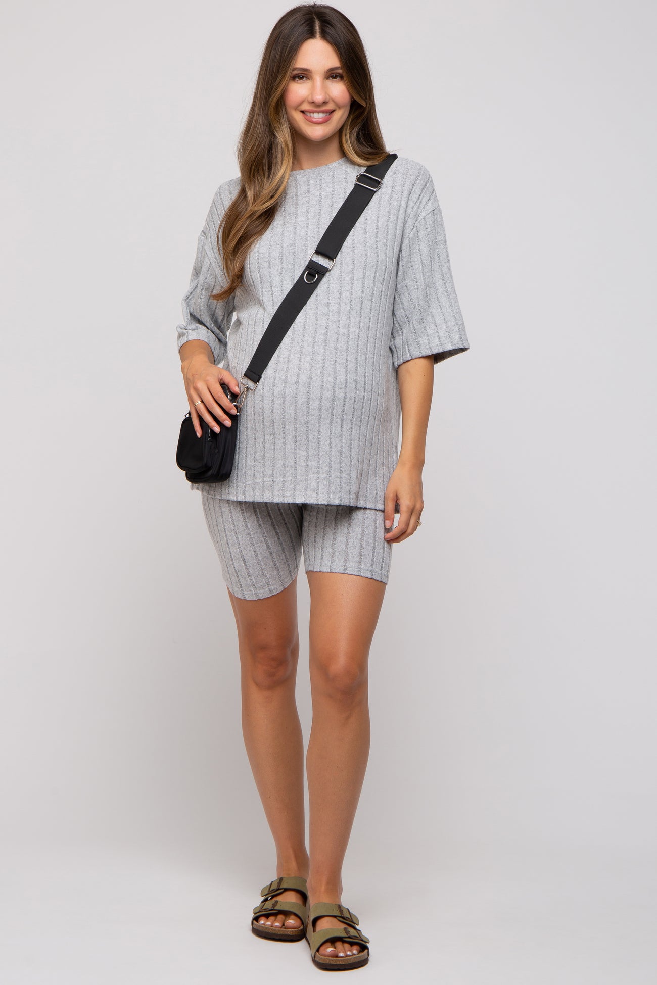woman wearing a gray ribbed maternity short set with a loose top and shorts, holding a small bag and standing confidently