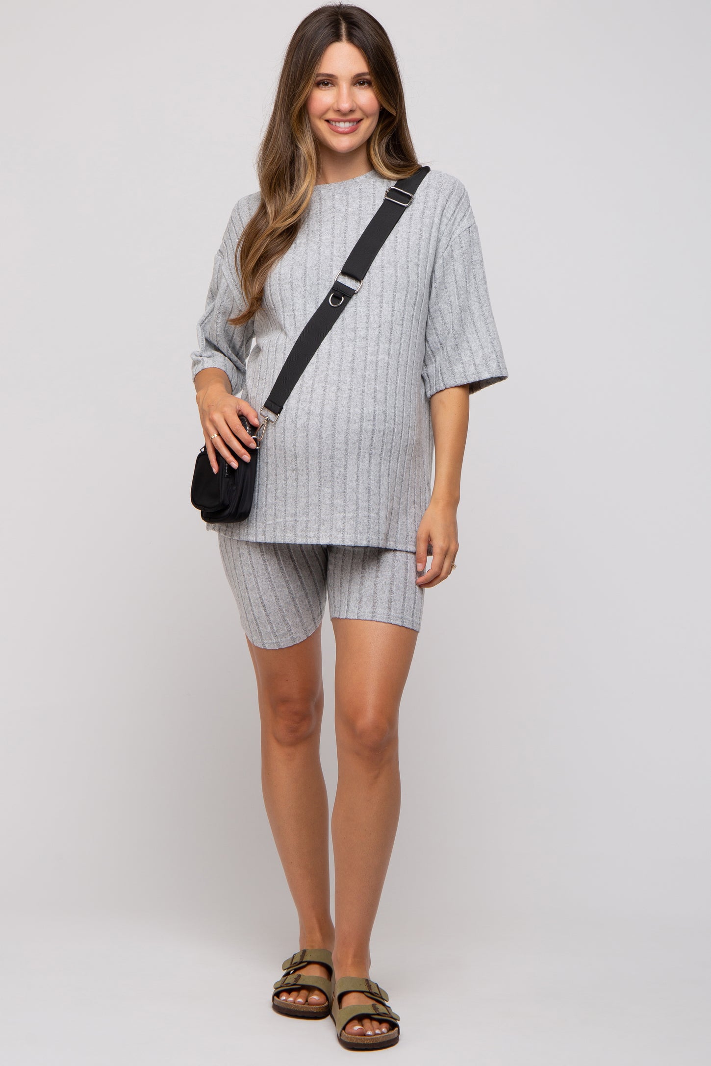 woman wearing a gray ribbed maternity short set with a loose top and shorts, holding a small bag and standing confidently